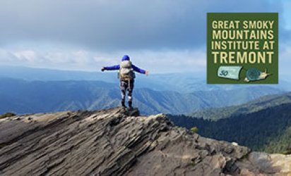 View of a person with a hiker's backpack standing almost center frame at the top of rock formation, the lines of which all point up diagonally from the bottom left towards the person center-frame. This person stands with their back to the viewer, arms outstretched, taking in a panoramic view of the Great Smoky Mountains unfolding before them: green close up, gradually turning more blue and blue as the lines of mountains recede into the distance. Clouds above. Logo in top right.